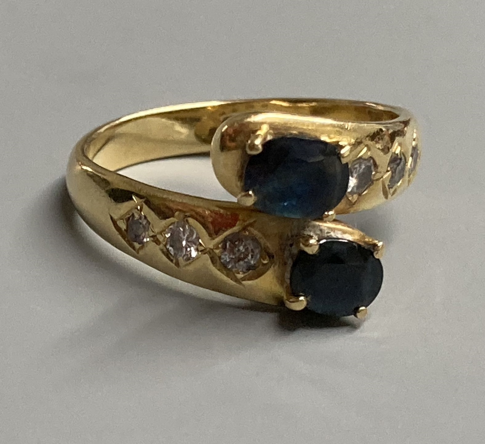 A modern 18ct and two stone sapphire crossover ring, with diamond set shoulders, size P, gross 5.4 grams.
